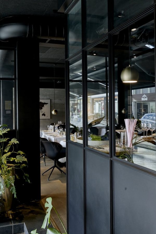 20. Entré til bistro lavet med skillevæg med sorte fyldninger i bunden og klart hærdet glas i toppen 20. Entré til bistro lavet med skillevæg med sorte fyldninger i bunden og klart hærdet glas i toppen